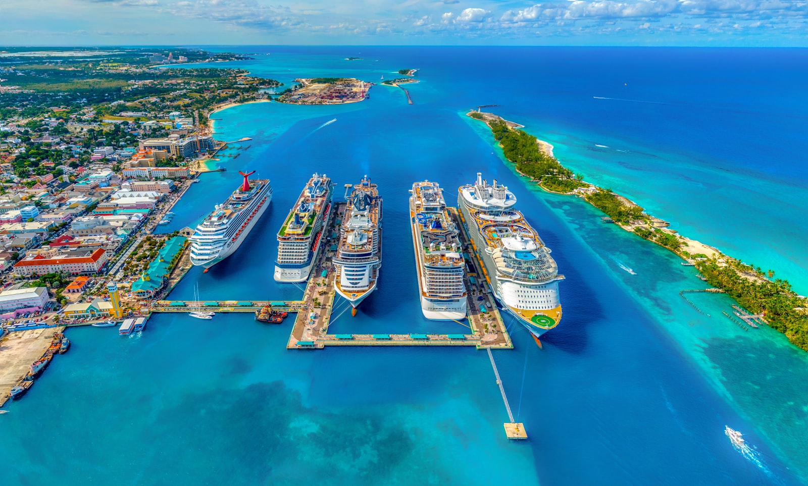 Cruise ships docked at a turquoise Bahamas port beside a palm-lined island